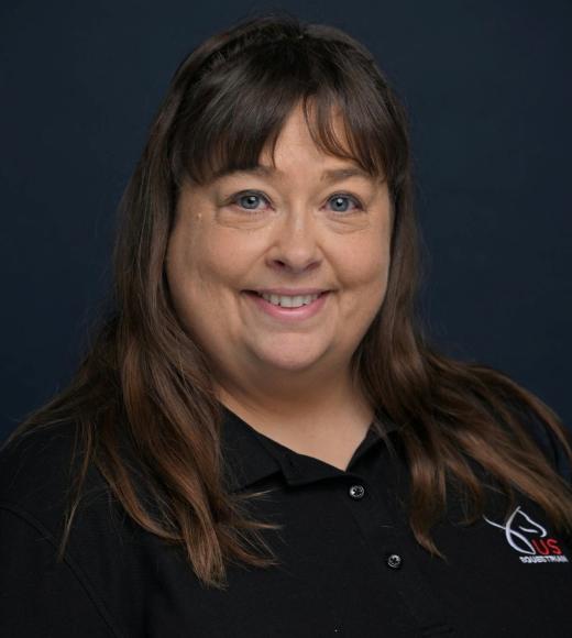 Smiling woman with brown hair wearing a black polo against a dark blue background